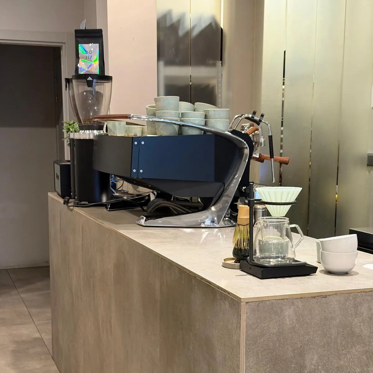 The stone-clad bar at Dosis with its espresso machine, a pour-over station and stacks of pale green Dosis cups