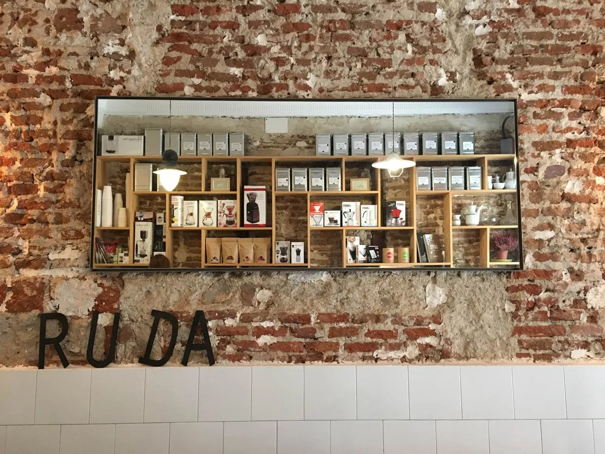 An exposed brick wall at Ruda Café with the RUDA letters beneath a lit shelf of coffee bags and brewing gear