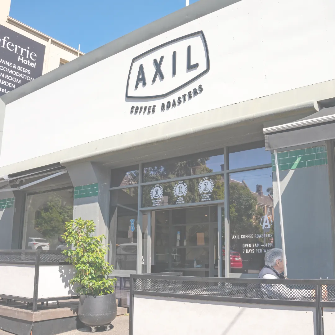 The white shopfront of Axil Coffee Roasters in Hawthorn, with the oval Axil sign above the glass doors and a potted plant on the terrace