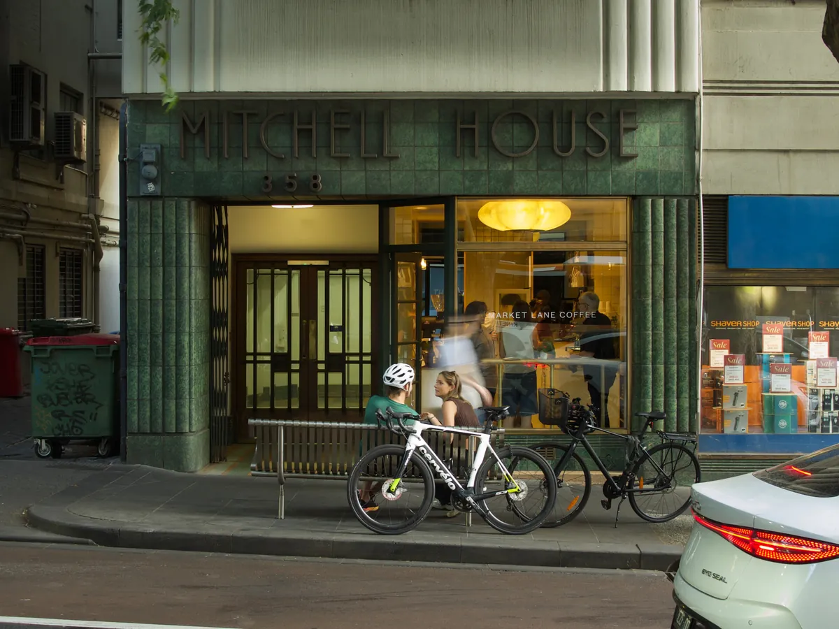 The green-tiled Art Deco entrance of Mitchell House in the CBD, with Market Lane Coffee's lit shop beside the doorway and bicycles parked out front