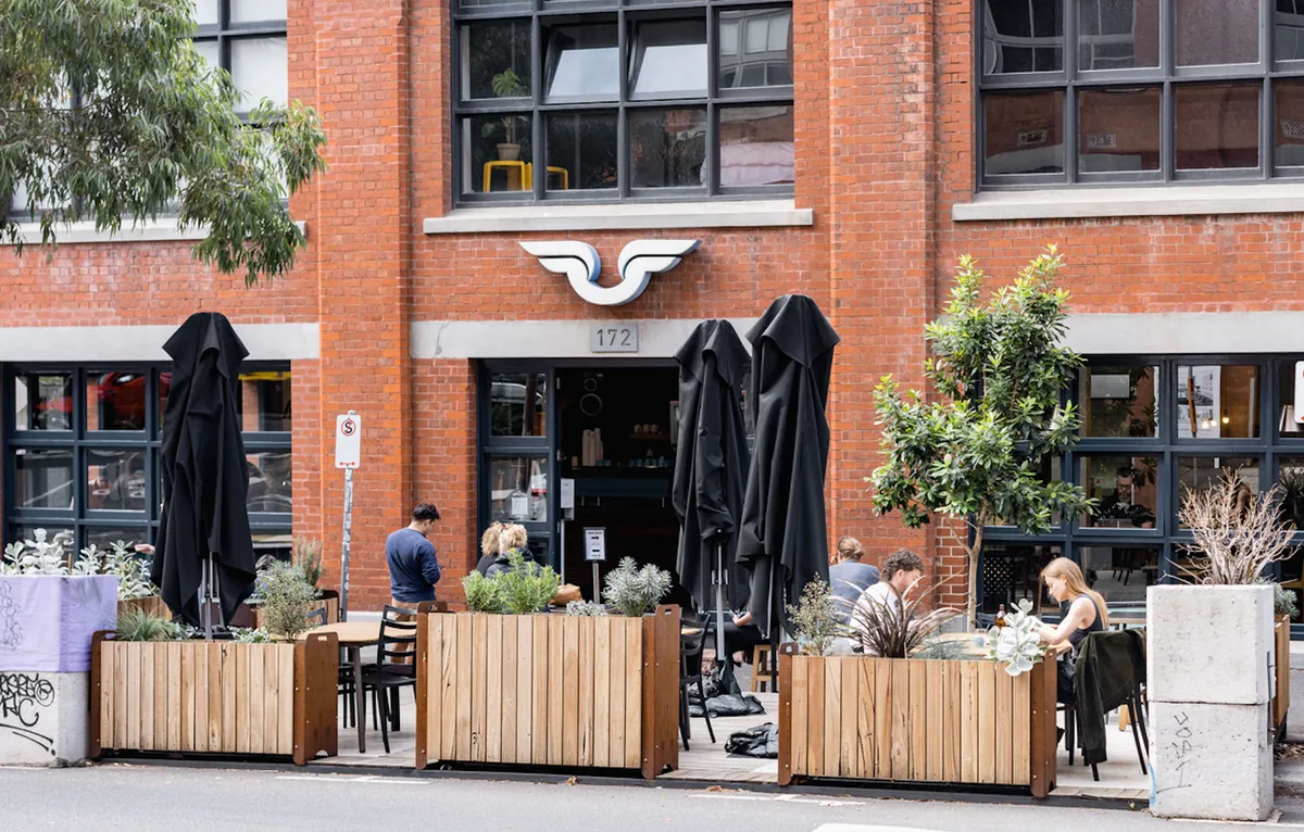 The red-brick front of Proud Mary in Collingwood, with closed black umbrellas and timber planters around the footpath seating