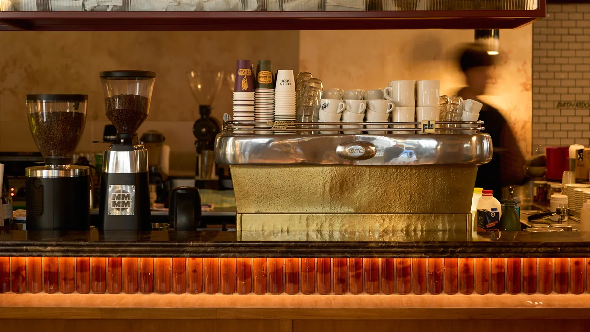 The espresso bar at ST. ALi South Melbourne, with a brass espresso machine, two grinders and stacked cups above a softly lit amber counter