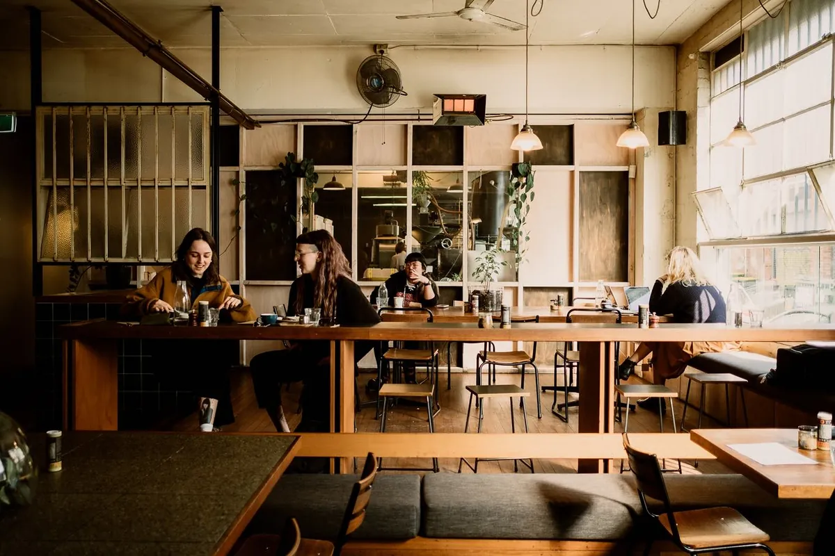 The dining room at Wide Open Road in Brunswick, with a long timber bench table, hanging pendant lights and tall factory windows