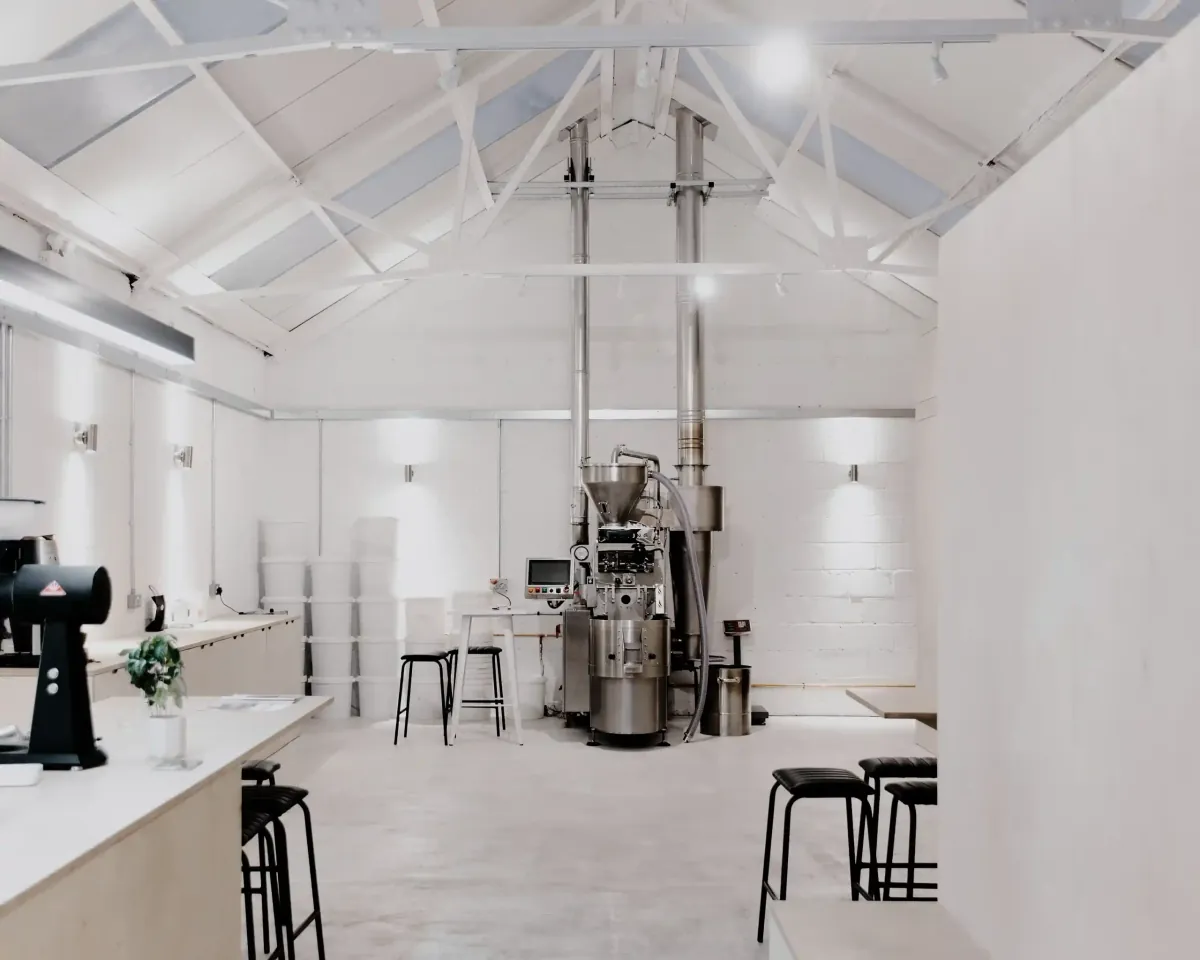 The white-painted NewGround Workshop roastery café in Headington, with the roaster under the pitched roof and stools along the counters