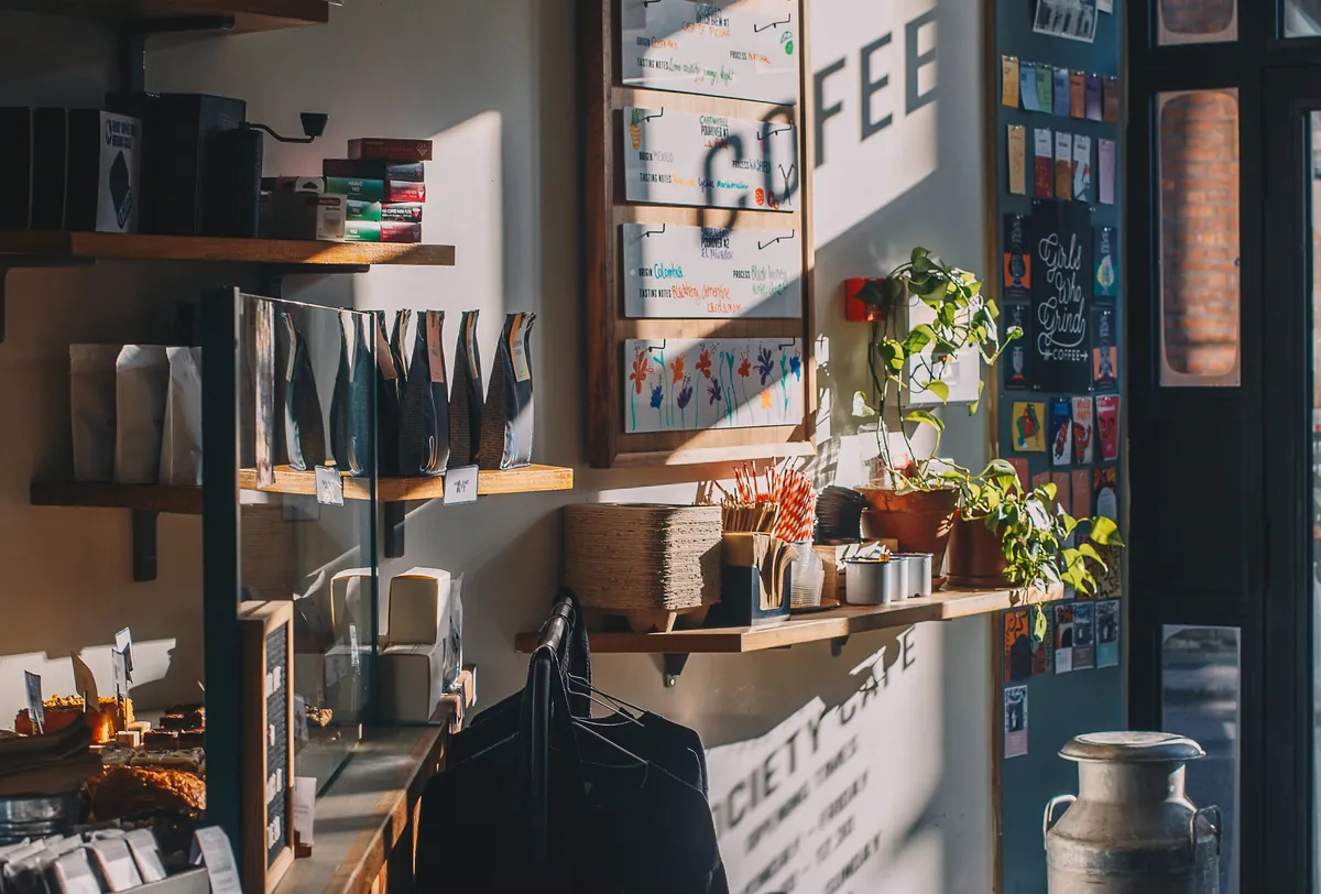 Low sun across shelves of coffee bags and plants beside the painted Coffee sign inside Society Café in Oxford