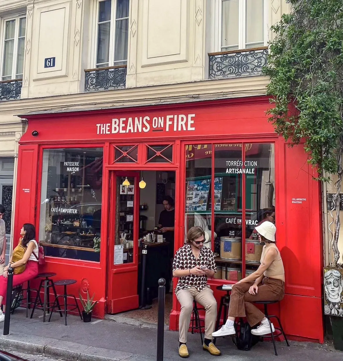 The red shopfront of The Beans on Fire in Montmartre, with customers on stools outside and the bar visible through the open door