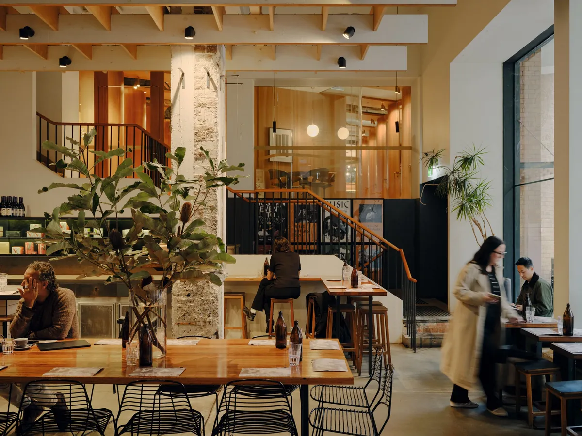 The dining room of Paramount Coffee Project in Surry Hills, with timber tables, a sandstone pillar and a staircase rising to a timber-lined mezzanine