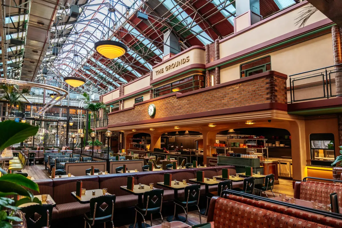 The dining hall of The Grounds Coffee Factory in the Locomotive Workshop at South Eveleigh, with booth seating under a glass roof and The Grounds sign above the bar