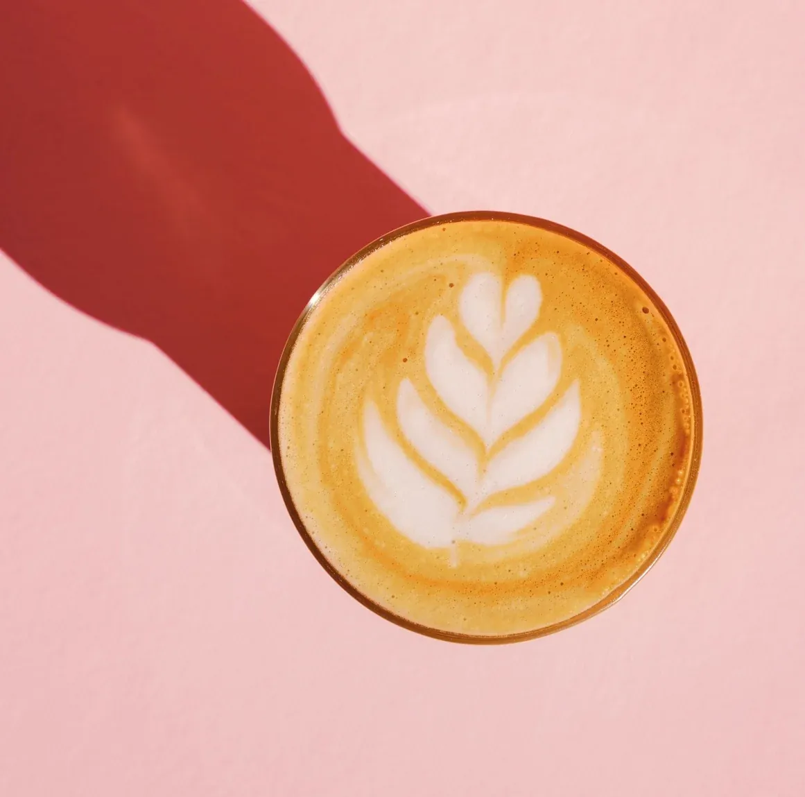 A latte with rosetta latte art in a glass on a pink table at Miffie's Coffee