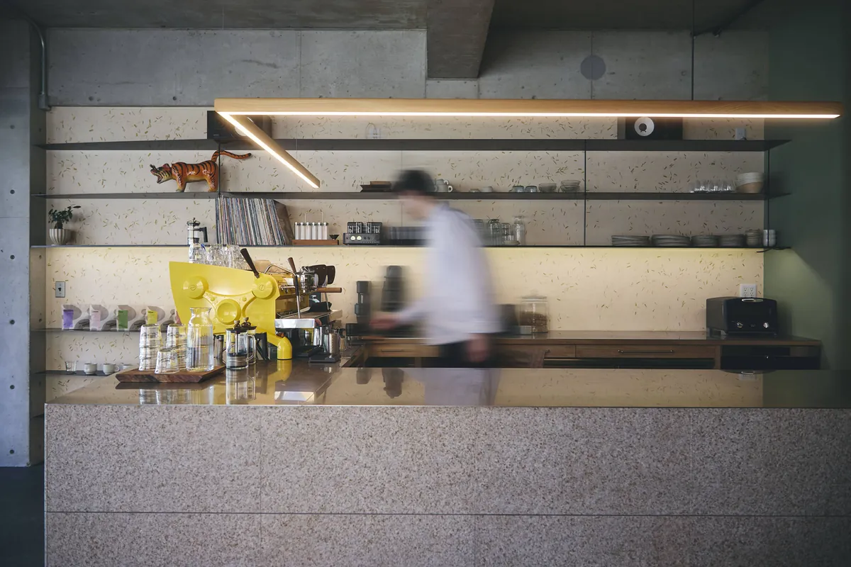 The terrazzo counter at SUNNY GEORGE under a long strip light, with a yellow espresso machine, grinders and open shelves on a plastered wall